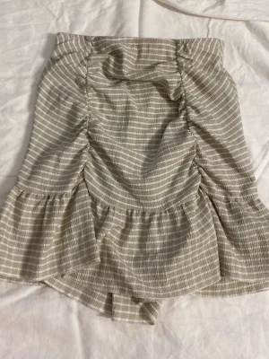 Beige kortkjol med volang från Gina Tricot - Supersöt beige och vit randig kortkjol från Gina Tricot. Kjolen har volang nertill och rynkade detaljer framtill och baktill som ger en trendig look