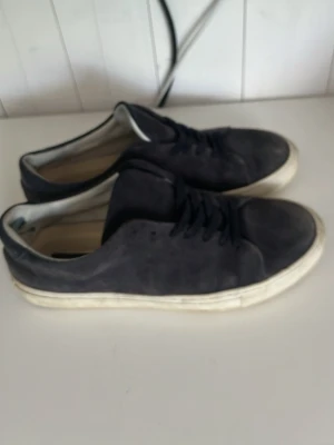 Sneaky Steve skor - Snygga mörkblå sneakers från Sneaky Steve i mocka med vita sulor. Klassisk låg modell med snörning och stilren design som passar till det mesta. Perfekta för dig som gillar en enkel men trendig look.