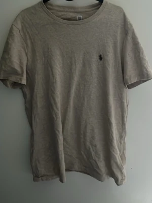 Beige t-shirt från Polo Ralph Lauren - Snygg beige t-shirt från Polo Ralph Lauren med klassisk rund hals och diskret logga broderad på bröstet. Perfekt basic-plagg i mjuk bomull som passar till allt. Enkel och stilren design med korta ärmar.