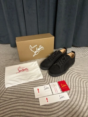 Svarta sneakers från Christian Louboutin - Stilrena svarta sneakers från Christian Louboutin med klassisk låg siluett. Skorna har ovandel i mocka och läder, svarta skosnören och diskret branding. Kommer med originalkartong, dustbag och äkthetskort. Perfekta för dig som gillar lyxiga och minimalistiska sneakers.