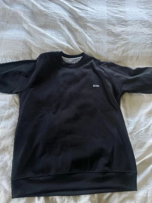 Svart sweatshirt från BOSS - En stilren svart sweatshirt från BOSS med rund halsringning och diskret logga på bröstet. 