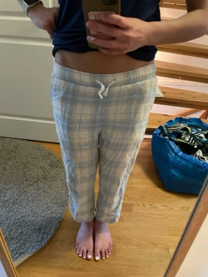 Rutiga pyjamasbyxor med snörning - Mysiga pyjamasbyxor i ljusa färger med rutigt mönster och snörning i midjan. Byxorna är 10-12 år och är perfekta för chill hemma. Materialet känns mjukt och luftigt, troligen bomull. Snyggt mönster i blått, beige och vitt.