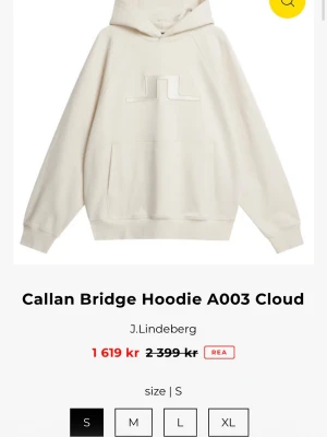 Vit hoodie J.Lindeberg Callan Bridge - Snygg vit hoodie från J.Lindeberg, modell Callan Bridge. Hoodien har en stor broderad logga på bröstet, känguruficka och huva. Tillverkad i mjukt material som känns skönt mot huden. Perfekt för en avslappnad och trendig stil.
