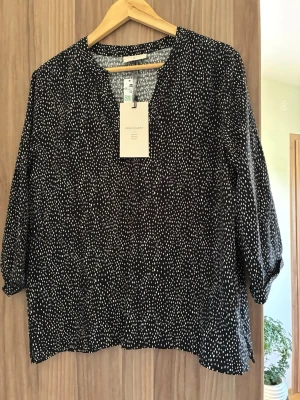 Svartvit blus från Freequent - Svart blus med vita prickar från Freequent. Modellen har trekvartsärm och en avslappnad passform med rund halsringning. Tunt och lätt material som känns skönt mot huden. Perfekt att styla med jeans eller kjol.