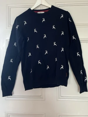Mörkblå sweatshirt med renar - Mörkblå sweatshirt med vita broderade renar över hela tröjan. Rund halsringning och långa ärmar. Perfekt för dig som gillar lekfulla detaljer och vill sticka ut lite extra. Mjuk och bekväm bomullskänsla.