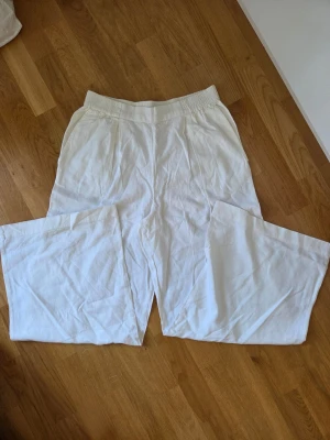 Vita vida linnebyxor med resårmidja - Snygga vita linnebyxor med breda ben och resår i midjan. Byxorna har en avslappnad passform och är tillverkade i ett lätt och luftigt linnematerial, perfekt för varma dagar. Klassisk look som är enkel att matcha med olika toppar.