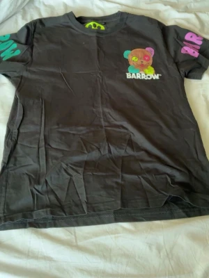 Svart Barrow t-shirt med färgglatt tryck - Cool svart t-shirt från Barrow med färgglatt nalletryck på bröstet och logga i vitt. Ärmarna har tryck i turkos och rosa. Rund halsringning och klassisk passform. Perfekt för dig som gillar streetwear och vill sticka ut.