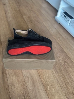 Svarta sneakers med röd sula - Stilrena svarta sneakers med ovandel i mockaliknande material och klassisk snörning. Skorna har en unik röd yttersula som ger en cool kontrast. Insidan är ljusbeige och designen är enkel men trendig, perfekt för dig som gillar en clean look.