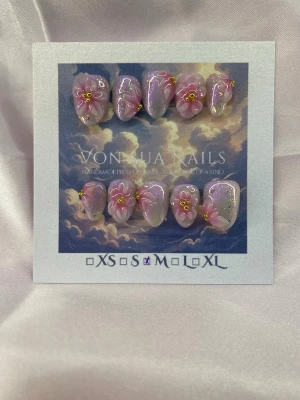 SakuraDrip (M);ExtraShortAlmond  - Handgjorda press-on naglar i storlek M: 16 mm, 12 mm, 12,5 mm, 11,5 mm, 10 mm. Naglarna har en pärlemor rosa bas med skimrande glitter och dekorerade 3D-blommor i rosa och vitt med gula detaljer. Extra korta och Mandelformade och unika, perfekta för dig som vill sticka ut med en kreativ och söt nageldesign.