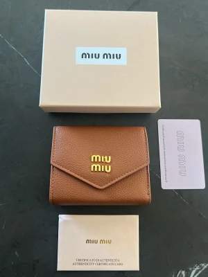 Brun plånbok från Mi läder - Snygg brun plånbok från Mi med guldfärgad logotyp på framsidan. Plånboken har flera kortfack och ett myntfack, samt kommer med originalbox och autenticitetskort. Perfekt för dig som vill ha en stilren och lyxig accessoar.