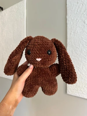 Brun virkad kanin  - Virkat gosedjur i velvetgarn. Kaninen är 26cm lång och tillverkad för hand, vilket gör varje kanin unik. Kaninen har svarta säkerhetsögon som sitter fast från insidan. Rekommenderas dock inte för de allra minsta barnen, då det alltid finns en viss risk, vid hårt drag, att de lossnar. Perfekt som present eller mysig inredningsdetalj! Tvättråd: max 30°C, handtvätt.