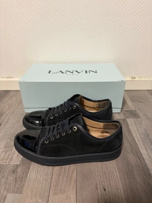 Lanvin - Stilrena blåa sneakers från Lanvin med snygg kontrast mellan mocka och lackad tå. Klassisk låg modell med blåa skosnören och diskreta metalldetaljer. Perfekta för dig som gillar exklusiv och minimalistisk design.