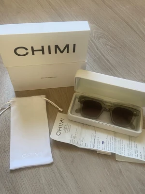 Chimi glasögon gråa - Snygga solglasögon från CHIMI i transparent grå färg med fyrkantiga bågar. Kommer med originalförpackning, kvitto fodral och putsduk. Perfekta för dig som vill ha en stilren och modern accessoar. Tillverkade i acetat och perfekta för sommaren