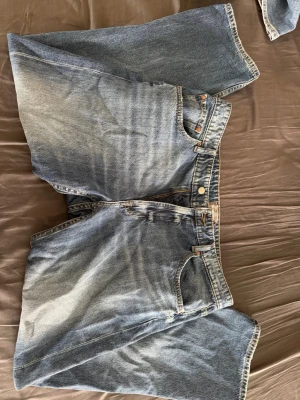 Blå raka jeans med vintage tvätt - Säljer ett par blå jeans med rak passform och snygg vintage tvätt. Klassisk femficksmodell med dragkedja och knapp i midjan. Jeansen har en ljusare tvätt framtill och bakfickor med enkel design. Perfekta för en avslappnad stil.