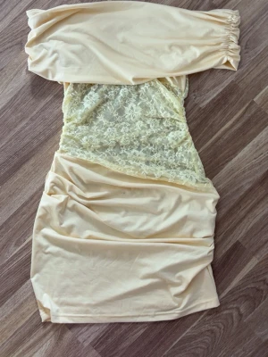 Ljusgul offshoulder spetsklänning - Trendig ljusgul kortklänning med offshoulder-modell och transparent spetsdetalj över magen. Klänningen har en figurnära passform och är perfekt för dig som vill sticka ut. Materialet är mjukt och bekvämt, med elastiska partier upptill.