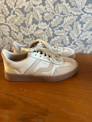 Beige sneakers från GANT - Säljer då de inte passar, så därav endast använda 2-3 gånger!💕 Snygga beige sneakers från GANT med klassisk låg profil och bruna sulor. Skorna har en kombination av läder och mocka, samt vita snören och diskret GANT-logga i guld på sidan. Perfekta för dig som gillar stilrena och trendiga sneakers.