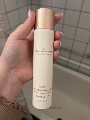 Rituals Purify Cleansing Balm - Rituals The Ritual of Namaste Purify Radiant Glow Cleansing Balm med moringa och sötmandelolja. Flaskan är krämvit med guldfärgat lock och elegant minimalistisk design. Perfekt för dig som vill ha en lyxig rengöring i badrumshyllan.