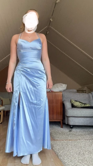 Jättefin ljusblå balklänning med slits och korsett knyttning - Jättefin ljusblå balklänning med slits och en liknande korsetknytning i ryggen som gör att ryggen är helt öppen. Den är använd en gång på 9 ans bal. Den har inga defekter och är i nytt skick. Den går att att knyta åt precis som på en korsett så den sitter enligt din figur. Köpt ny för 2000kr. Säljer den då jag inte har nån användning för den längre. Passar perfekt till 9:ans bal, student, bröllop eller nåt annat liknande.🩵🩵🩵