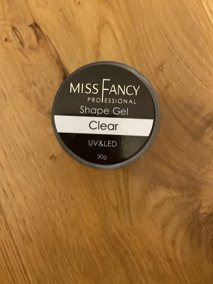 Miss Fancy Shape Gel Clear 30g - Miss Fancy Professional Shape Gel Clear är en genomskinlig nagelgel för UV och LED-lampa. Perfekt för att bygga och forma naglar med en naturlig finish. Burken innehåller 30g gel som är enkel att applicera och ger ett snyggt resultat.