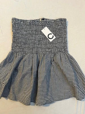 Svartvit rutig kortkjol från Cubus - Trendig kortkjol från Cubus i svartvitt rutigt mönster. Kjolen har smock upptill som ger en bekväm och snygg passform, samt en volang nedtill för extra stil. Perfekt för dig som gillar en cool och avslappnad look.