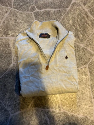Ljusbeige stickad tröja Morris - Säljer en ljusbeige stickad tröja från Morris i 100% merinoull. Tröjan har halv dragkedja, hög krage och en liten broderad logga på bröstet. Perfekt för dig som gillar stilrena och klassiska plagg. Den kan se lite skrynklig ut för att den ej är använd på ett tag