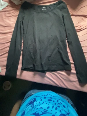 Svart långärmad topp från 157 - En enkel och stilren svart långärmad topp från 157 med rund halsringning. Perfekt att matcha med jeans eller kjol. Materialet känns mjukt och lätt, troligen bomull eller polyester. Snygg passform som sitter normalt på kroppen.
