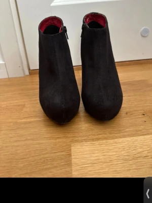 Svarta pumps från Vox Shoes  - Snygga svarta pumps från Vox Shoes med spetsig tå och dragkedja på sidan. Skorna har en röd innersida och är tillverkade i mockaliknande material. Perfekt för dig som vill ha en stilren och elegant look.