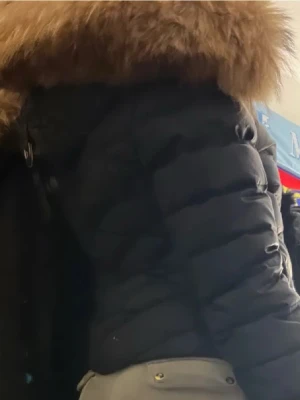 Holliejacka med äkta päls  - Snygg svart Äkta hollie pufferjacka med stor luva kantad av beige äkta päls . Jackan har dragkedja framtill, två sidofickor och quiltad design som är perfekt till nästa höst vinter. Perfekt för kalla vinterdagar och riktigt varm tack vare den tjocka vadderingen. Inköpt för 4200 kr en gång i tiden . Storlek 36/S. Kan mötas upp i Helsingborg/Malmö annars tillkommer frakt . Kan gå ner i pris vid snabb äffär. I bra skick endast 1 liten liten skada där bak men går att fixa enkelt. 