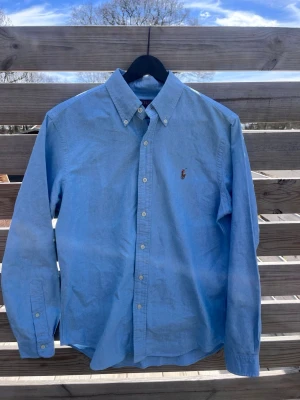 Blå skjorta från Polo Ralph Lauren - Hej! Vi säljer nu en ljusblå skjorta från Polo Ralph Lauren med button-down krage och broderad logga på bröstet. Skjortan har långa ärmar och vita knappar framtill. Perfekt till jeans eller chinos för en clean och stilren look. Nyskick på denna extremt fina skjortan och storlek S men passar även M. Skjortan kostar 379kr pga det extremt bra skicket, nypris på den ligger någonstans runt 1600kr men går att sänka vid snabb och smidig affär.💙