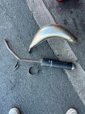 Tecnigas E-Nox till am6 - Säljer ett avgassystem till moped, med böjd silverfärgad expansion och svart ljuddämpare. Inkluderar fäste och skruvar. Materialet är metall och systemet har en sportig design som passar till mopeder och mindre motorfordon.