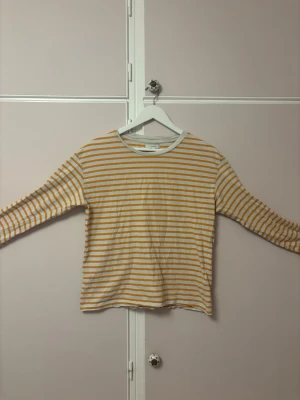 Randig långärmad topp från Lindex - Säljer en långärmad topp från Lindex med vita och oreanga ränder. Toppen har en klassisk rund halsringning och är gjord i mjuk bomull. Perfekt för en avslappnad och stilren look. Sista bilden visar färgen tydligast. 