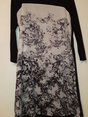 Svartvit blommig långärmad klänning - En stilren klänning med svart överdel och ärmar samt vit front med svart blommigt mönster. Klänningen har en rak form och är långärmad, perfekt för dig som gillar grafiska kontraster och blommiga detaljer. Materialet känns mjukt och följsamt. Storlek L