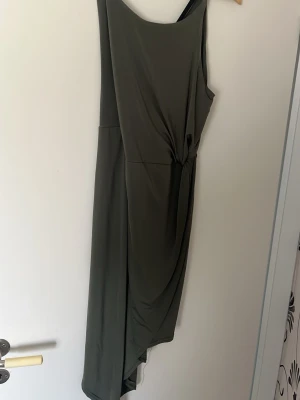 Grön långklänning från Atmosphere - Säljer en snygg grön långklänning från Atmosphere med asymmetrisk skärning och draperad detalj på sidan. Klänningen är ärmlös och har en enkel, stilren design som passar perfekt för dig som gillar minimalistiskt mode.