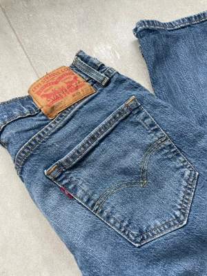 Levi's 505 blå jeans loose straight - Klassiska Levi's 505 jeans i blå denim med raka ben och femficksdesign. Jeansens bakficka har den ikoniska röda Levi's-taggen och läderpatch på linningen. Materialet är slitstark bomullsdenim och passformen är tidlös och avslappnad.