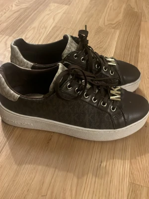 Michael Kors skor - Snygga bruna sneakers från Michael Kors med guldfärgad MK-logga på tån och mönstrad ovandel. Skorna har vita kanter och en låg profil. Perfekt för dig som vill ha en trendig och stilren look. Pris kan diskuteras vid snabba köp! 🤗