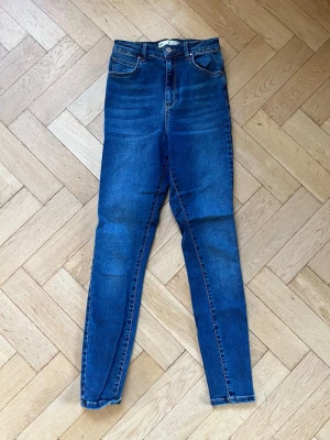 Blå high waist skinny jeans - Säljer ett par blå skinny jeans med hög midja och klassiska femficksdetaljer. Jeansen har en snygg tvätt med lätt slitning och är tillverkade i stretchigt denim. Från Gina Tricot i modellen Gina.