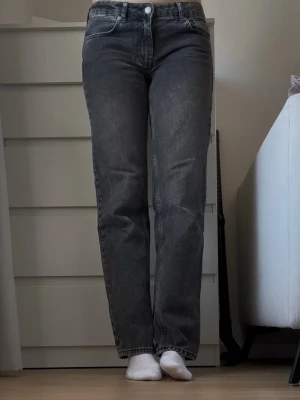 Mörkgrå raka jeans med hög midja - Säljer ett par mörkgrå jeans med rak passform och hög midja. Jeansen har klassiska fem fickor och knappstängning framtill. Materialet är denim och färgen är en snygg tvättad grå som passar till många olika stilar.