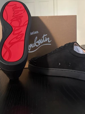 Svarta Louboutin sneakers spikar - Säljer ett par svarta sneakers från Christian Louboutin med mattsvarta spikar på tån och klassisk röd sula. Skorna har en stilren design i mocka med svarta snören och detaljer. Perfekta för dig som vill sticka ut med exklusiva detaljer. Helt nytt skick aldrig använda!