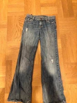 Blå bootcut jeans med broderad ficka - Säljer ett par blå bootcut jeans med slitningar och snyggt broderi på bakfickan. Jeansen är ifrån GAP och i storlek 14 slim. 
