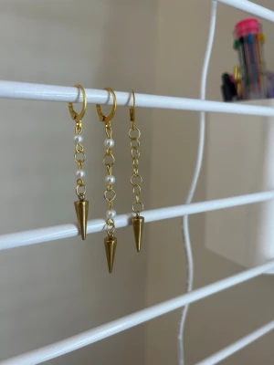 Guldpläterade örhängen med pärlor - Säljer 3 coola guldpläterade örhängen med kedjor, små vita pärlor och spetsiga hängande koner. Perfekt för dig som gillar edgy och trendiga accessoarer. Örhängena har en unik design med både metall och pärldetaljer. Handgjort 