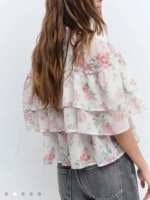 Blommig volangblus  - Somrig blus från gina med volanger och blommigt mönster i rosa och grönt på vit bakgrund. Använd endast 2 gånger. 