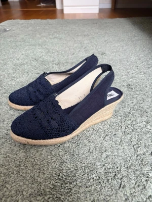 Marinblå kilklackssandaler  - Snygga marinblå sandaler från Bellezza med kilklack i flätad jute och öppen häl. Ovandelen är i tyg med virkade detaljer och spetsmönster.