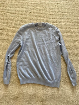 Ljusblå stickad tröja från Bläck - Snygg ljusblå stickad tröja från Bläck med rund halsringning och ribbade muddar vid ärmslut och nederkant. Perfekt för lager på lager och enkel att matcha med olika outfits. Tillverkad i mjukt material för skön känsla.