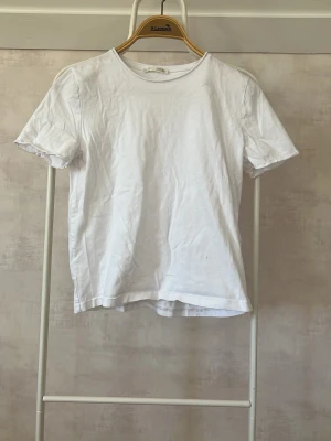 Vit basic t-shirt i bomull - Klassisk vit t-shirt i mjuk bomull med rund hals och korta ärmar. Perfekt till jeans eller shorts för en enkel och clean look. Passformen är normal och tyget är tunt och skönt.