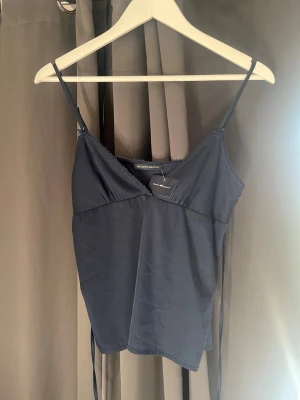 Mörkblå linnetopp från Brandy Melville  - Snygg mörkblå linnetopp från Brandy Melville med tunna axelband och dekorativ knytning i ryggen. Toppen har en lätt v-ringad halsringning och är tillverkad i ett mjukt, lent material som känns skönt mot huden. Perfekt att styla med jeans eller kjol.