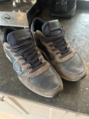 Philippe Model grå/blåa sneakers  - Snygga sneakers från Philippe Model i en mix av blå mocka och blått läder. Skorna har blåa skosnören, låg profil och en vit sula. Klassisk design med logga på sidan. Perfekta för dig som gillar stilrena och trendiga sneakers.