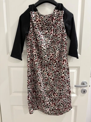 Leopardmönstrad klänning Soaked in Luxury - Snygg kort leopardmönstrad klänning från Soaked in Luxury med svarta trekvartsärmar. Klänningen har en lös passform och ett mjukt, glansigt tyg som ger en lyxig känsla. Perfekt för dig som vill sticka ut med ett djurmönster.