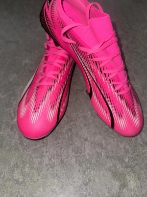  Fotbollsskor Puma - Säljer ett par riktigt snygga fotbollsskor i stark rosa färg med vita och svarta detaljer. Skorna har en strömlinjeformad design, tunn ovandel i syntetmaterial och klassisk snörning för bra passform. De är helt nya och oanvända.