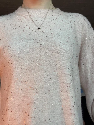 Ljusrosa stickad tröja med paljetter - Supersöt ljusrosa stickad tröja med små glittriga paljetter i blommönster över hela tröjan. Tröjan har rund halsringning och långa ärmar. Perfekt för dig som vill ha något extra i vardagen och gillar glitter.