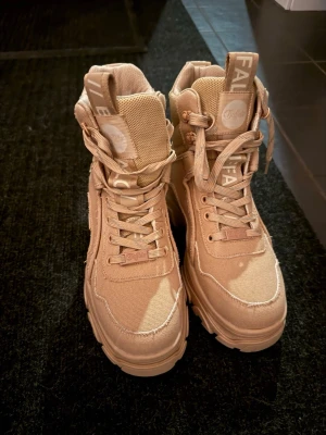 Beige kängor från Buffalo - Säljer ett par snygga beige kängor från Buffalo, endast använda vid 1 tillfälle ( testat dem) helt NYA med chunky sula och högt skaft. Kängorna har grova snören, detaljer i textil och mesh samt logga på plösen. Perfekta för dig som vill ha en street-inspirerad look och gillar robusta skor.